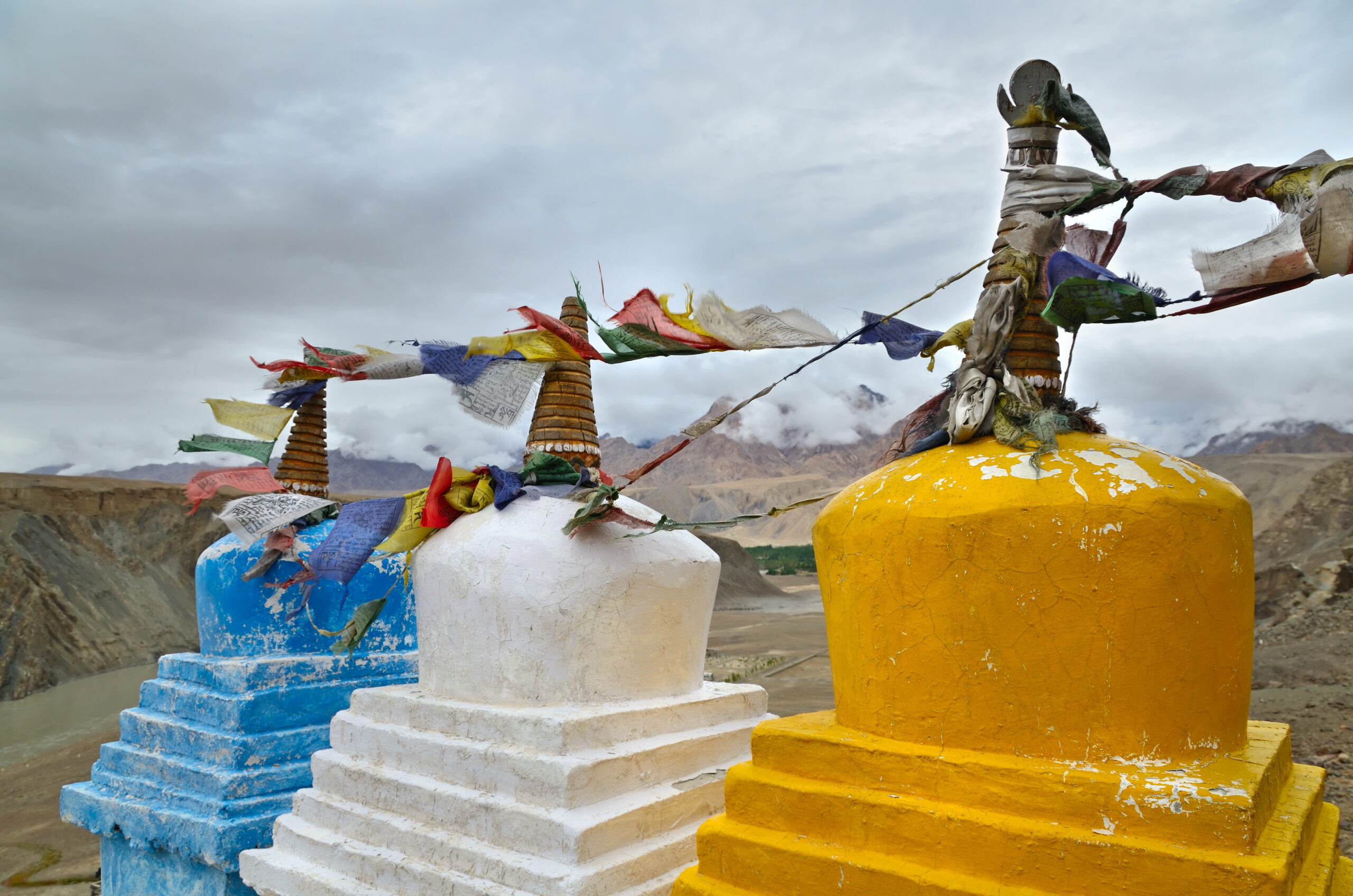 Buddhist chortens (stupas) with tibetan prayer flags near the confluence of the Indus and Zanskar rivers and Himalayas mountains on the background, Ladakh, India