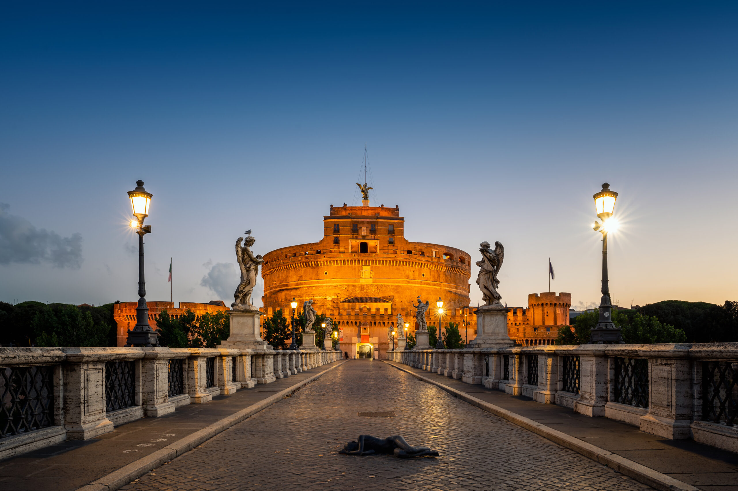 View of the illuminated Mausoleum of Hadrian, known as Castel Sant'Angelo from the Sant'Angelo bridge in blue hour before sunrise.