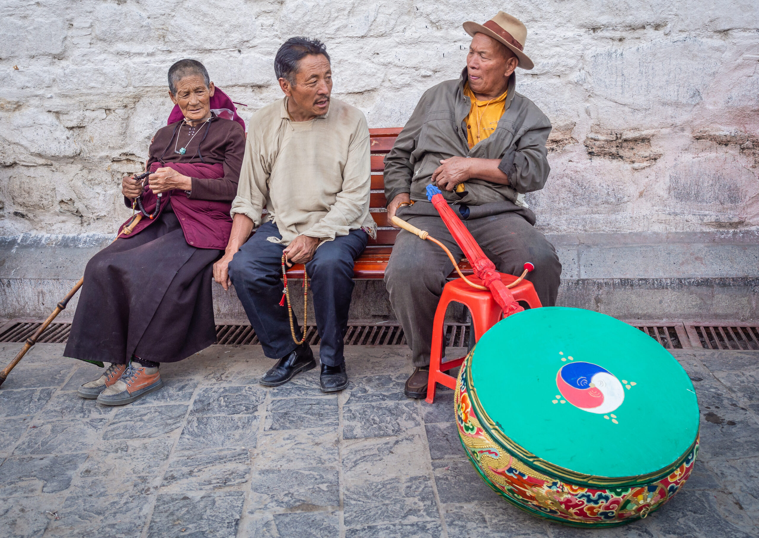 Tibet - August, 29 2014: Ethnic man and woman with beads looking at male with musical instrument while sitting on bench on town street