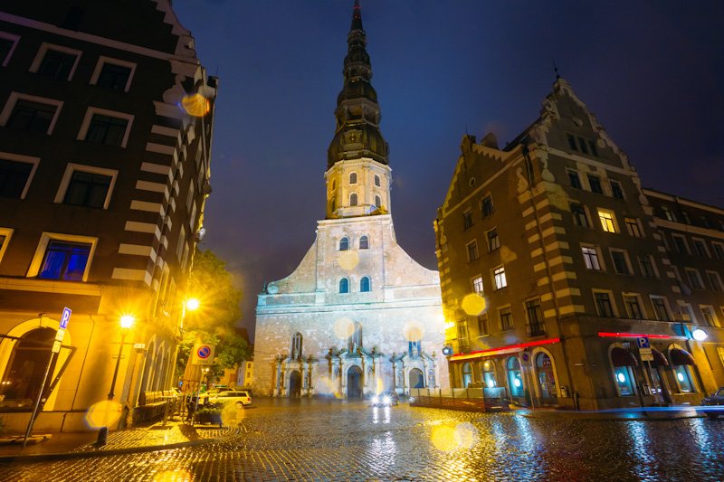 Riga Latvia. Night View Of Famous Landmark - St. Peter's Church In Old Town Riga Latvia. Illuminated Street. Famous Place