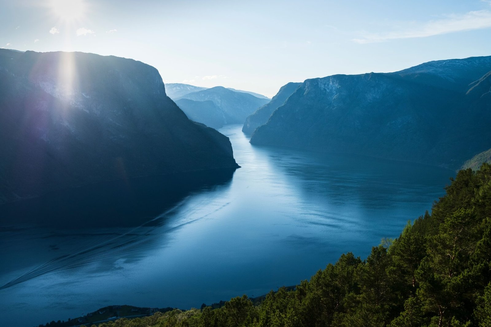 A stunning view of a fjord surrounded by mountains with the sun shining brightly in the sky.