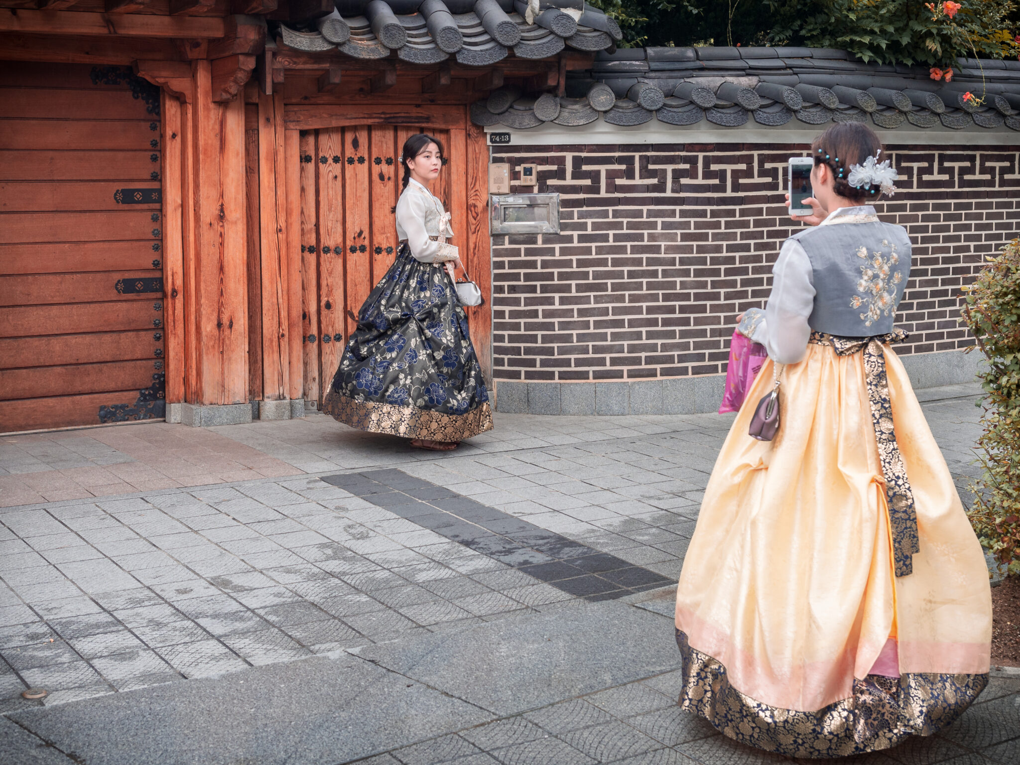 Jeonju, South Korea - August, 05 2017: Young Asian female taking picture of friend in traditional clothes on old town street