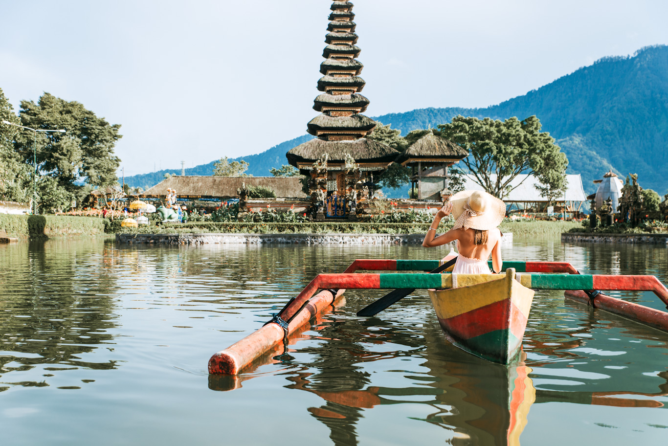 Young woman traveler paddling on a wooden boat at Pura Ulun Danu Bratan, Bali.