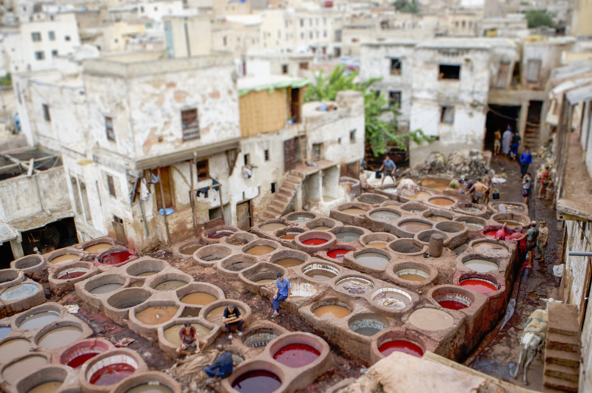 A bustling tannery with workers amidst vibrant dye pits in an ancient cityscape.